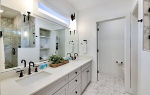 A modern bathroom with a large mirror, two sinks, and a shower area.