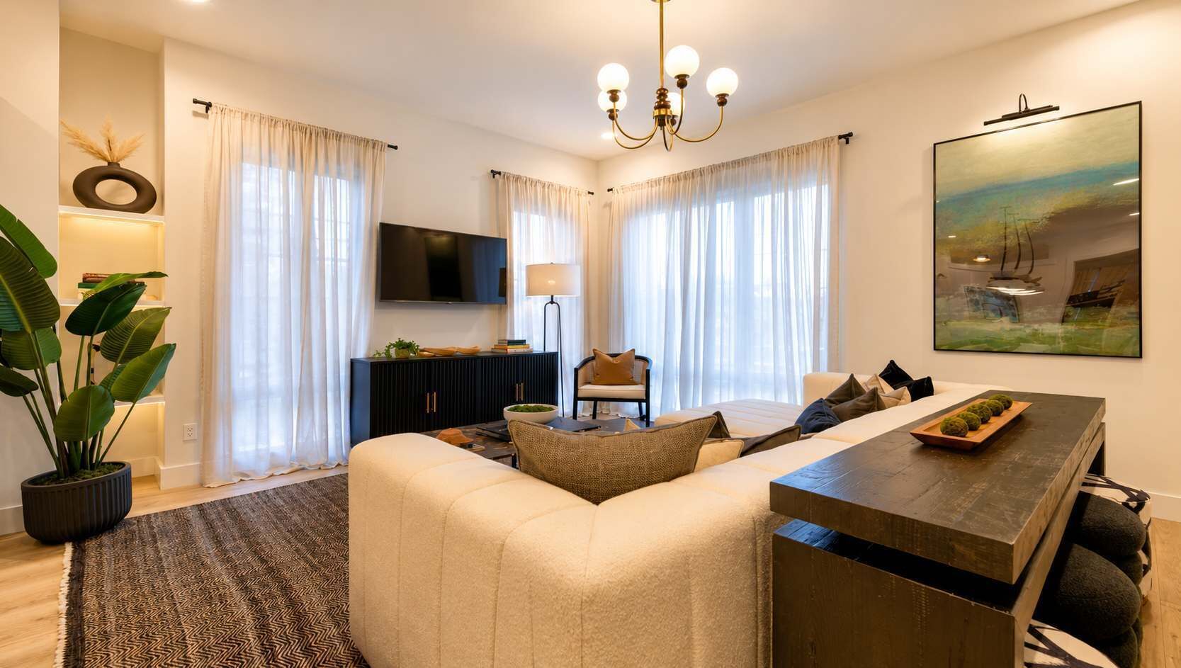 A modern living room with a sofa, a coffee table, and a TV. There is a potted plant and a painting on the wall.