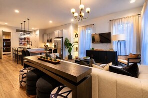A modern living room with a sofa, a dining area with a table, a kitchen with appliances, and a TV. - Nash Luxe Party! 13 Beds - Priv Hot Tub/Game Room! (Nashville)