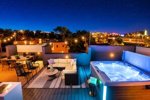 Une terrasse extérieure dotée d’un jacuzzi, d’un espace salon et de guirlandes lumineuses.