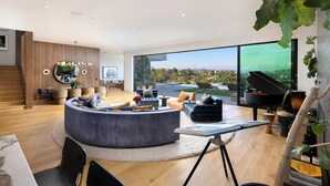 Una sala moderna con un ventanal grande, un rincón de estar circular, un piano y una mesa de comedor.