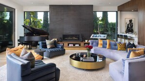 Una sala de estar moderna con un piano de cola, sofás, una chimenea y un ventanal grande.