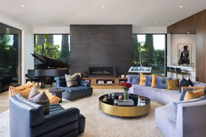 A modern living room with a grand piano, sofas, a fireplace, and a large window. - Dolce Vista - Bel Air Estate | 270° Views, Pool & Theater (Bel Air, Los Angeles)