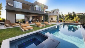 Una casa moderna de dos pisos con piscina, mobiliario exterior y vista al paisaje circundante.