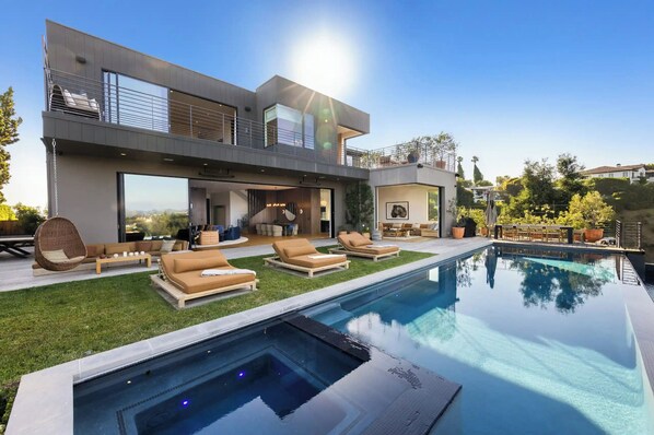 Une maison moderne à deux étages, dotée d’une piscine, d’un espace de détente extérieur et offrant une vue sur le paysage environnant.