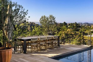 Une terrasse avec une table et des chaises, une piscine et une vue sur un paysage vallonné.