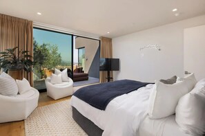 Un dormitorio con cama, televisión, sofá, silla y balcón con vistas.