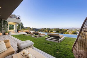 A modern outdoor patio with lounge chairs, a wooden deck, and a view of a lake and distant hills. - Dolce Vista - Bel Air Estate | 270° Views, Pool & Theater (Bel Air, Los Angeles)