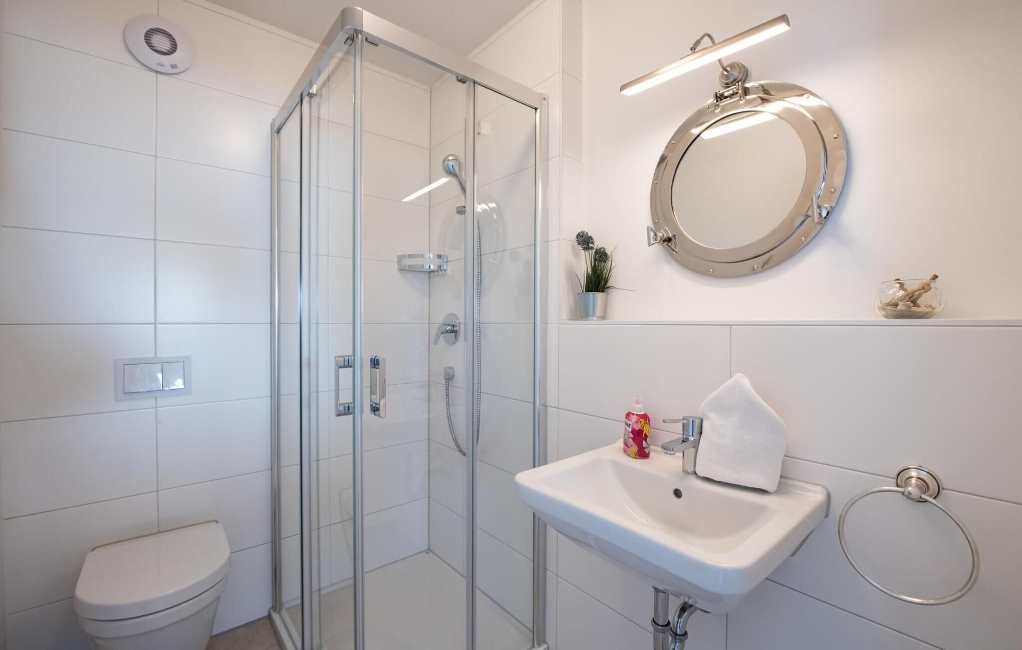 A modern bathroom with a glass shower enclosure, a white sink with a mirror above, and a toilet.