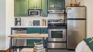 Una cocina con gabinetes verdes, un refrigerador de acero inoxidable, un microondas, una cafetera y una estufa.