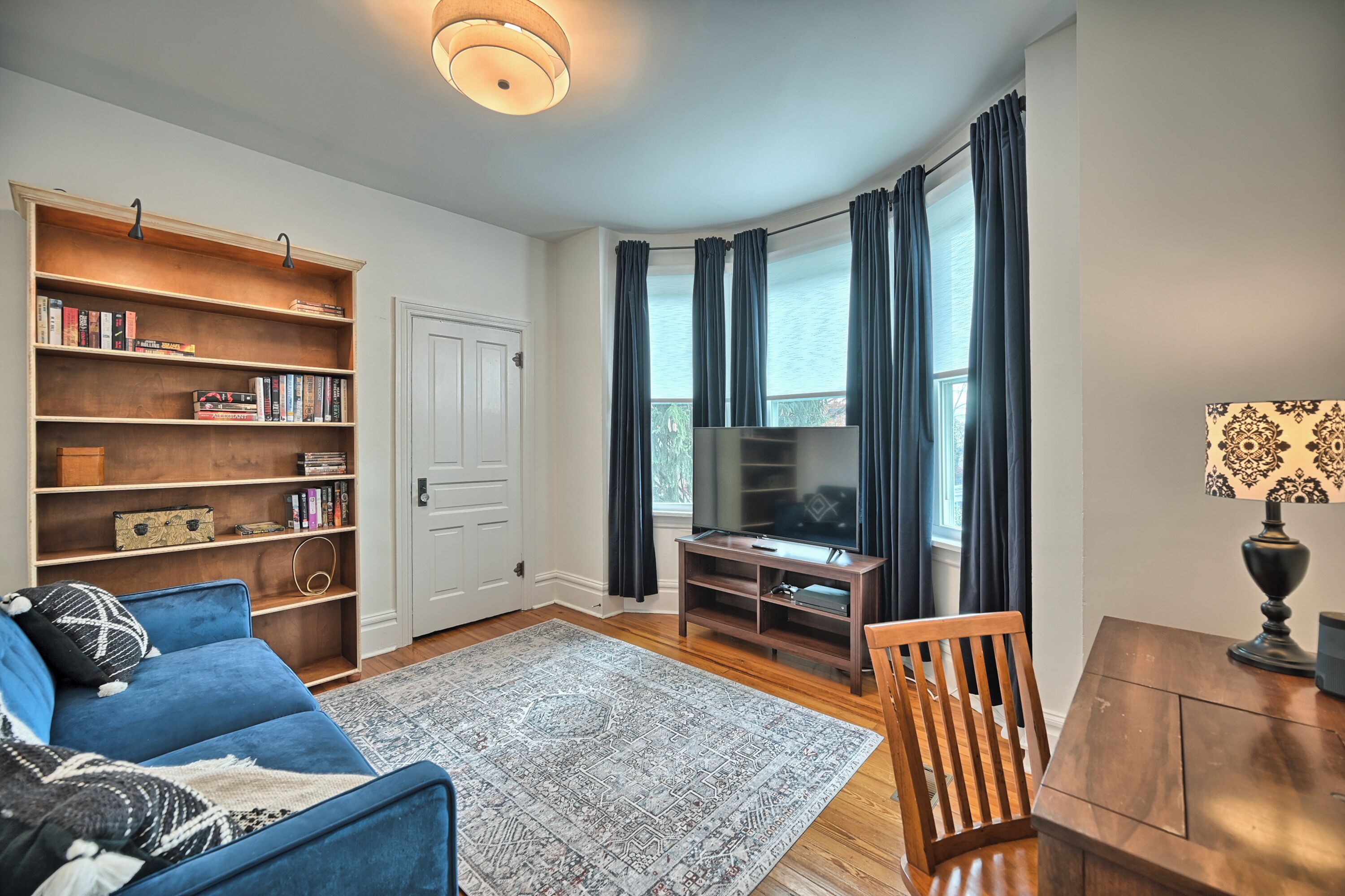 Een woonkamer met een blauwe bank, een houten boekenkast, een tv-meubel en een eettafel.