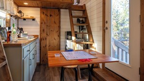 Una cocina acogedora con armarios de madera, una mesa de madera con un juego, una escalera y vistas a árboles por la ventana.