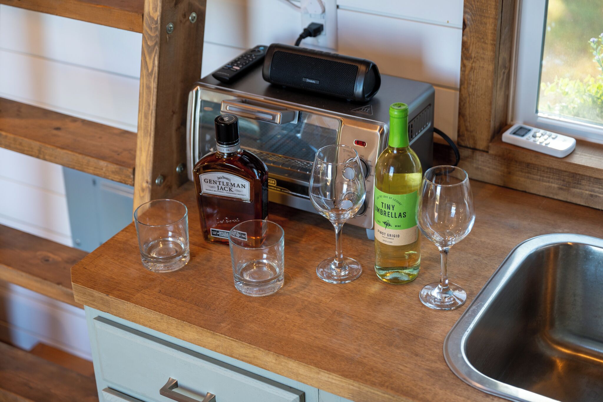 Una encimera de cocina con una botella de whisky, dos copas de vino, una botella de vino y un tostador.