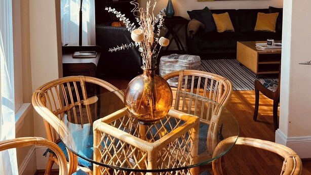 Ein Wohnzimmer mit Couch, Korbstühlen, einem Glastisch und einem Gemälde an der Wand.