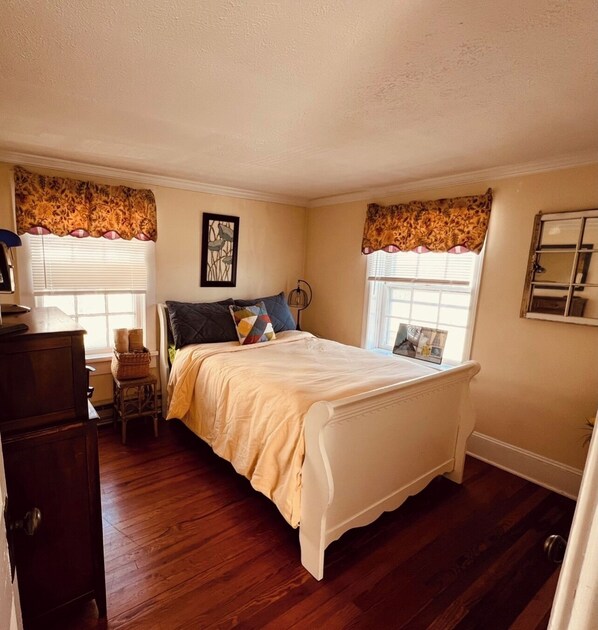 A bedroom with a bed, wooden floor, a dresser, and a window with curtains.
