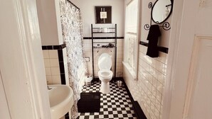 Ein schmales Badezimmer mit Schachbrettfußboden, Toilette, Waschbecken und Spiegel an der Wand.
