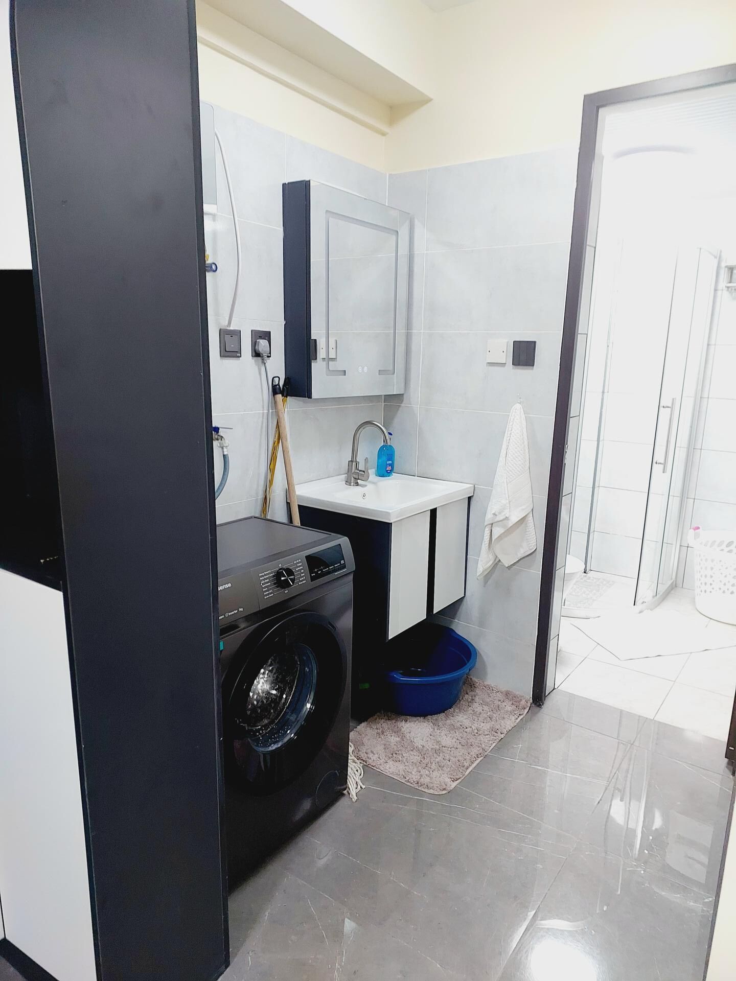 A compact bathroom with a washing machine, a sink, and a shower area.