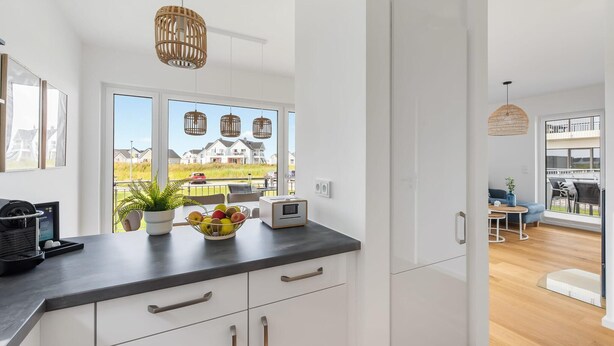 Eine moderne Küche mit weißen Schränken, einer schwarzen Arbeitsplatte und Blick auf Häuser durch große Fenster.
