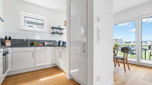 Eine moderne Küche mit weißen Schränken, einem Einbauofen und einem Fenster mit Blick auf einen Balkon.