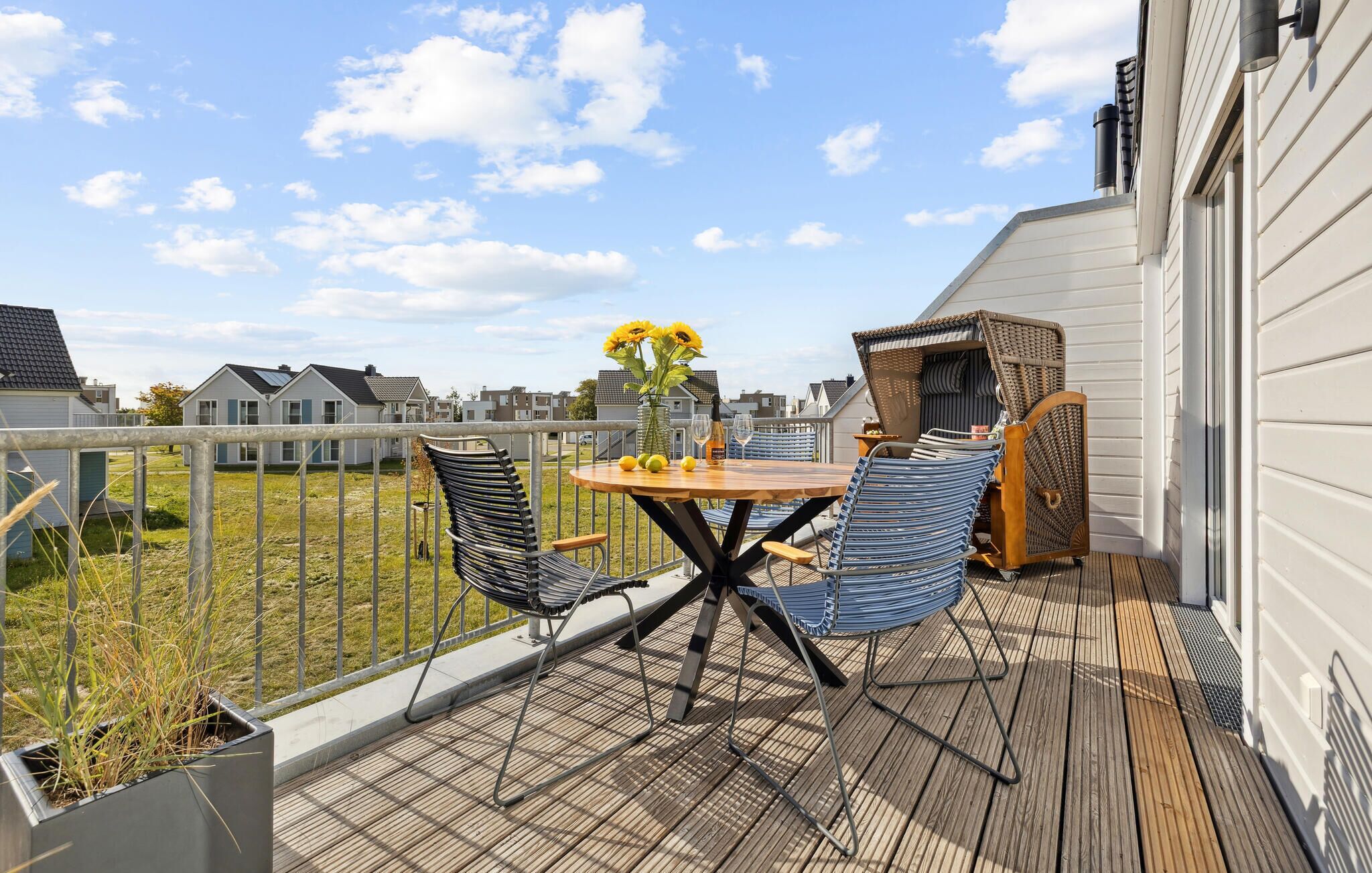 A balcony with a wooden table, two chairs, a vase with sunflowers, and a wicker chair.