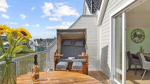 Un balcon avec une table en bois, deux chaises, un canapé et un vase rempli de tournesols.