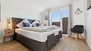 Une chambre moderne avec un grand lit, des tables de chevet, un fauteuil et une vue sur le ciel par une fenêtre.
