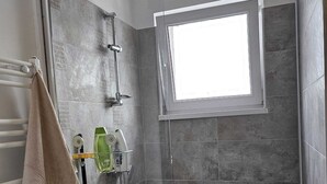 A small, modern bathroom with a built-in washing machine, a towel rack, and a shower with a window. - Garsoniera Gorjului (Bucharest)