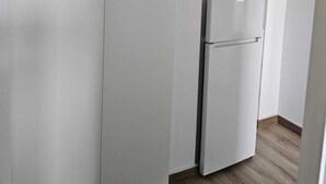 A narrow hallway with white walls and a wooden floor. A white refrigerator is positioned against the wall. - Garsoniera Gorjului (Bucharest)
