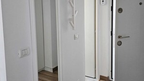 A hallway with white walls, a wooden floor, and a door with a key lock. There is a light switch and a power outlet on the wall. - Garsoniera Gorjului (Bucharest)
