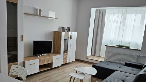 A modern living room with a sofa, TV, white cabinets, and a dining area. - Garsoniera Gorjului (Bucharest)