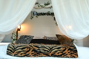 Een slaapkamer met een bed, witte gordijnen en een bordje aan de muur.