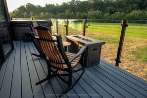 A deck with a rocking chair and a small table, overlooking a grassy field. - Tarzan And Jane Treehouse. Hot tub. Riverfront (Sevierville)