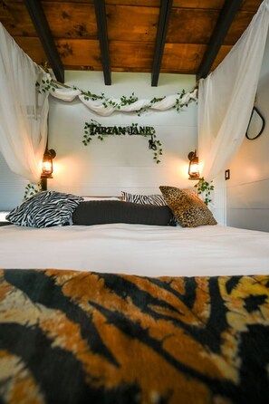 A bedroom with a bed, white curtains, a wall-mounted sign, and two wall-mounted lamps.
