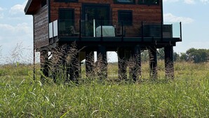 A wooden cabin with a balcony, situated in a grassy field. - Tarzan And Jane Treehouse. Hot tub. Riverfront (Sevierville)