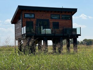 A wooden cabin with a balcony, situated in a grassy field. - Tarzan And Jane Treehouse. Hot tub. Riverfront (Sevierville)