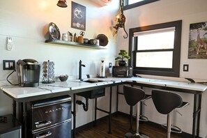 A modern kitchen with a coffee maker, microwave, and bar stools.
