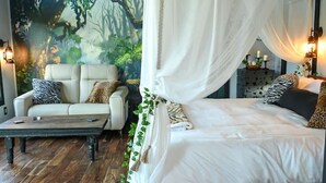 A bedroom with a canopy bed, a sofa, and a mural of a forest.