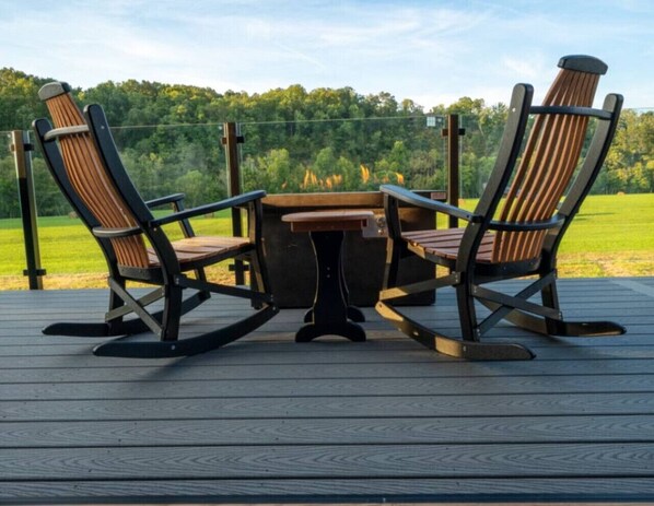 Une terrasse dotée de deux fauteuils à bascule et d’une table, offrant une vue sur une zone boisée.