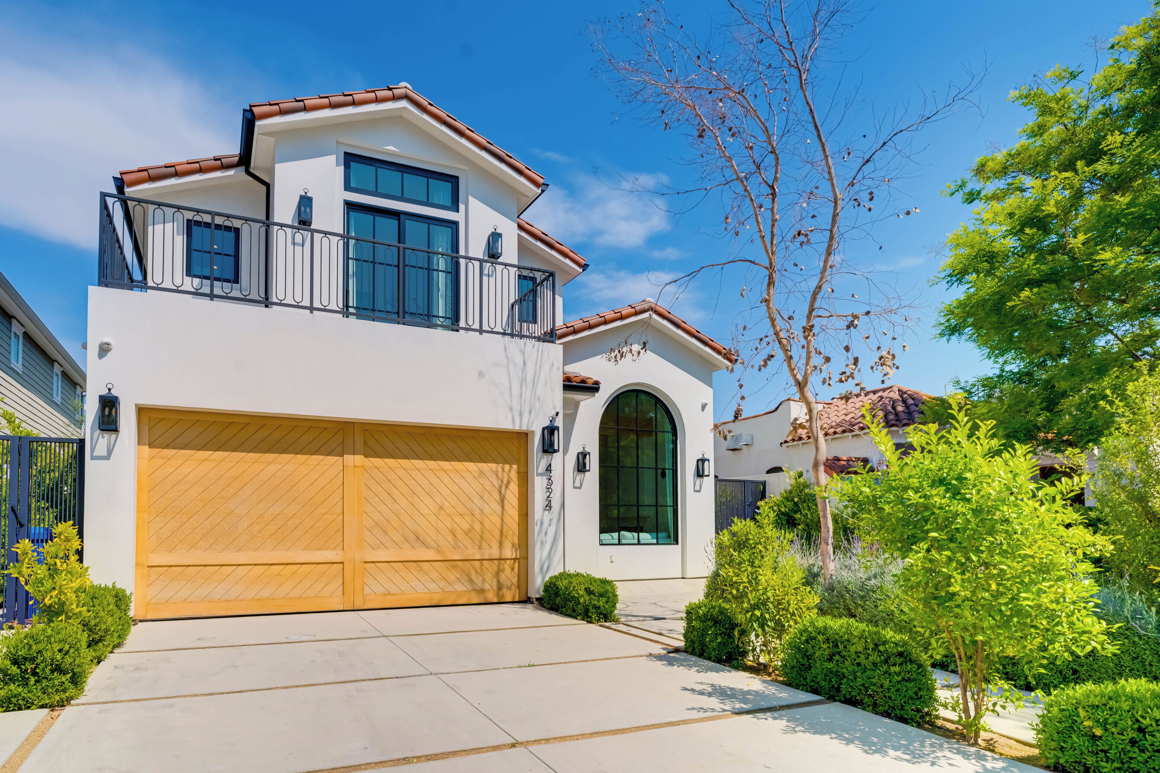 A modern two-story house with a large garage, a balcony, and a well-maintained garden.