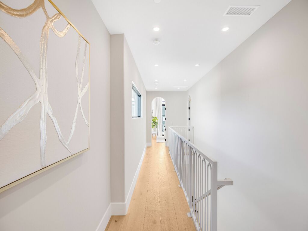 A hallway with a wooden floor, white walls, and a white railing.