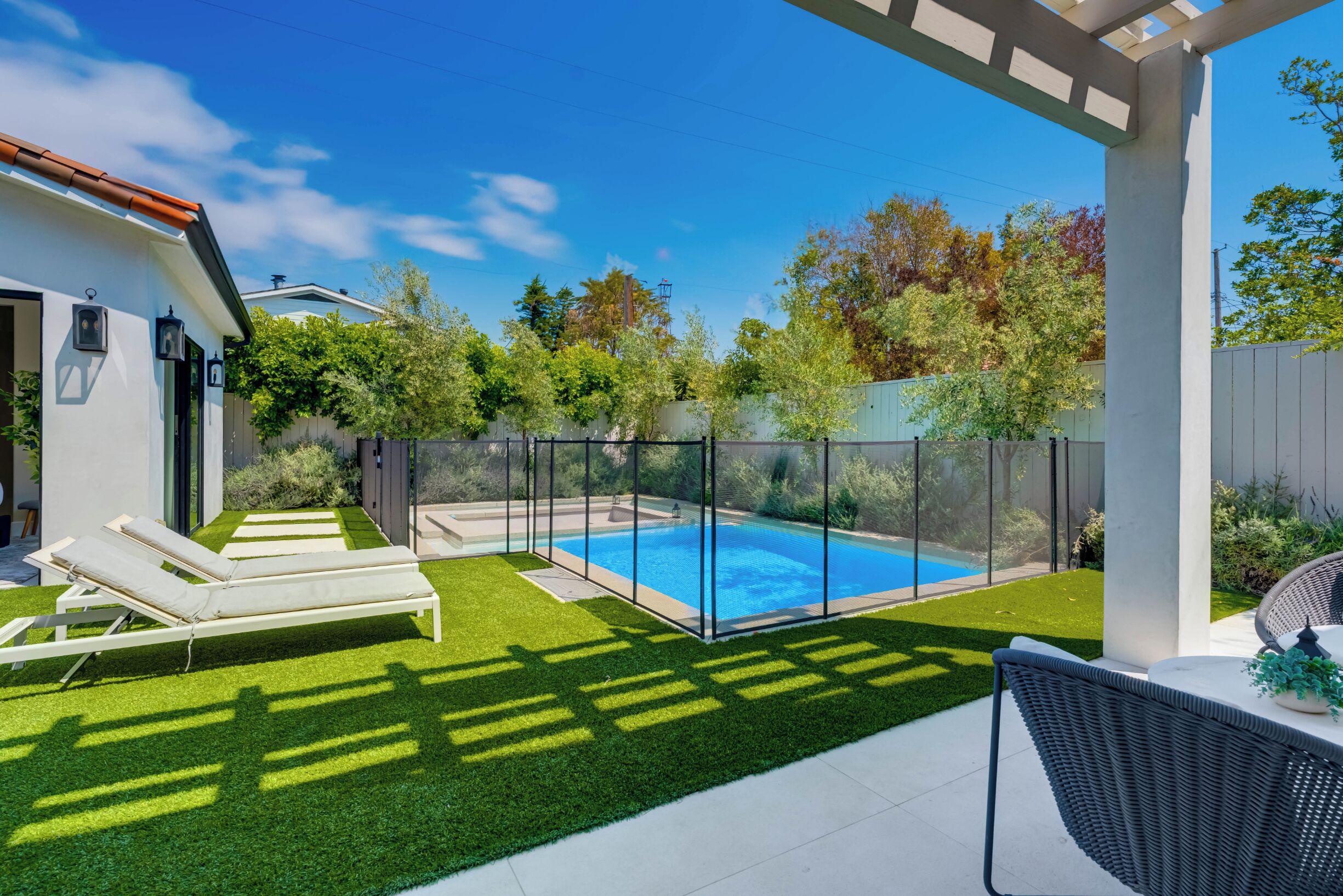 A backyard with a swimming pool, artificial grass, and lounge chairs.