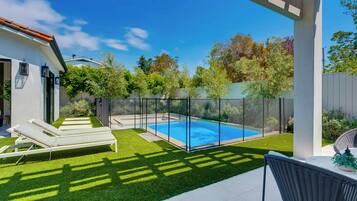 A backyard with a swimming pool, artificial grass, and lounge chairs.