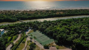 Ein Luftbild eines Küsteneigentums mit Tennisplatz, dichter Vegetation, einem Fluss und einem Strand.
