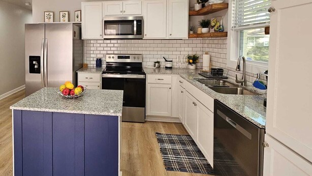 A modern kitchen with white cabinets, a central island, stainless steel appliances, and a window with blinds. - Charming 3-bedroom house in welcoming Hollywood/Meggett, SC. (Meggett)