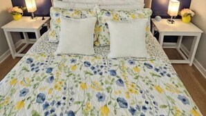 A bed with a floral duvet, two bedside tables with lamps, and a dark blue headboard. - Charming 3-bedroom house in welcoming Hollywood/Meggett, SC. (Meggett)