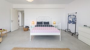 A modern bedroom with a white metal bed frame, a pink and white striped bedspread, a small bedside table with a lamp, and a wall-mounted radiator.