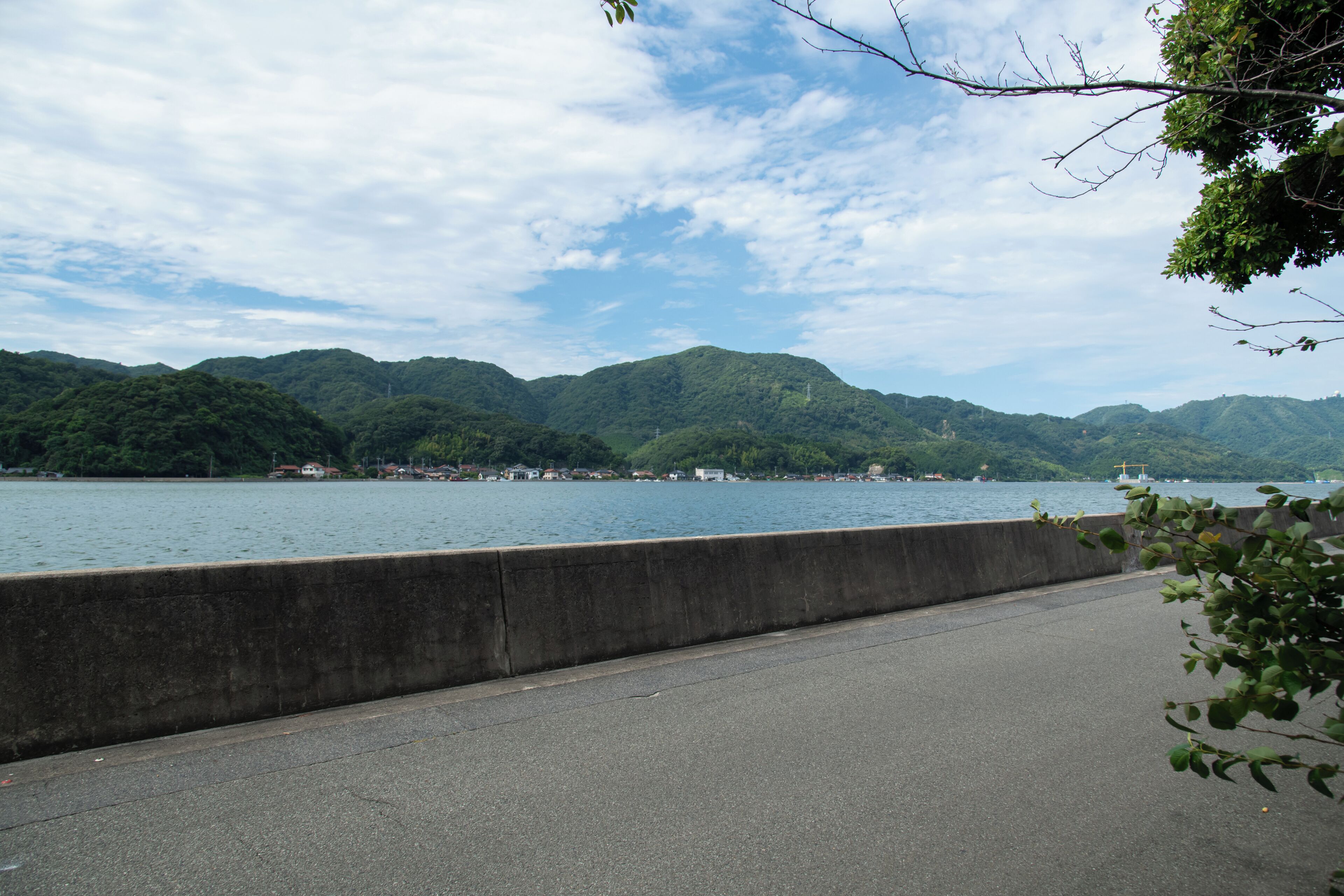 Een betonnen brug over het water, met bergen op de achtergrond.