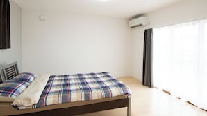 A room with a bed, a ceiling light, an air conditioning unit, and a window with curtains. - Destiny Seaside Village (Sakaiminato)