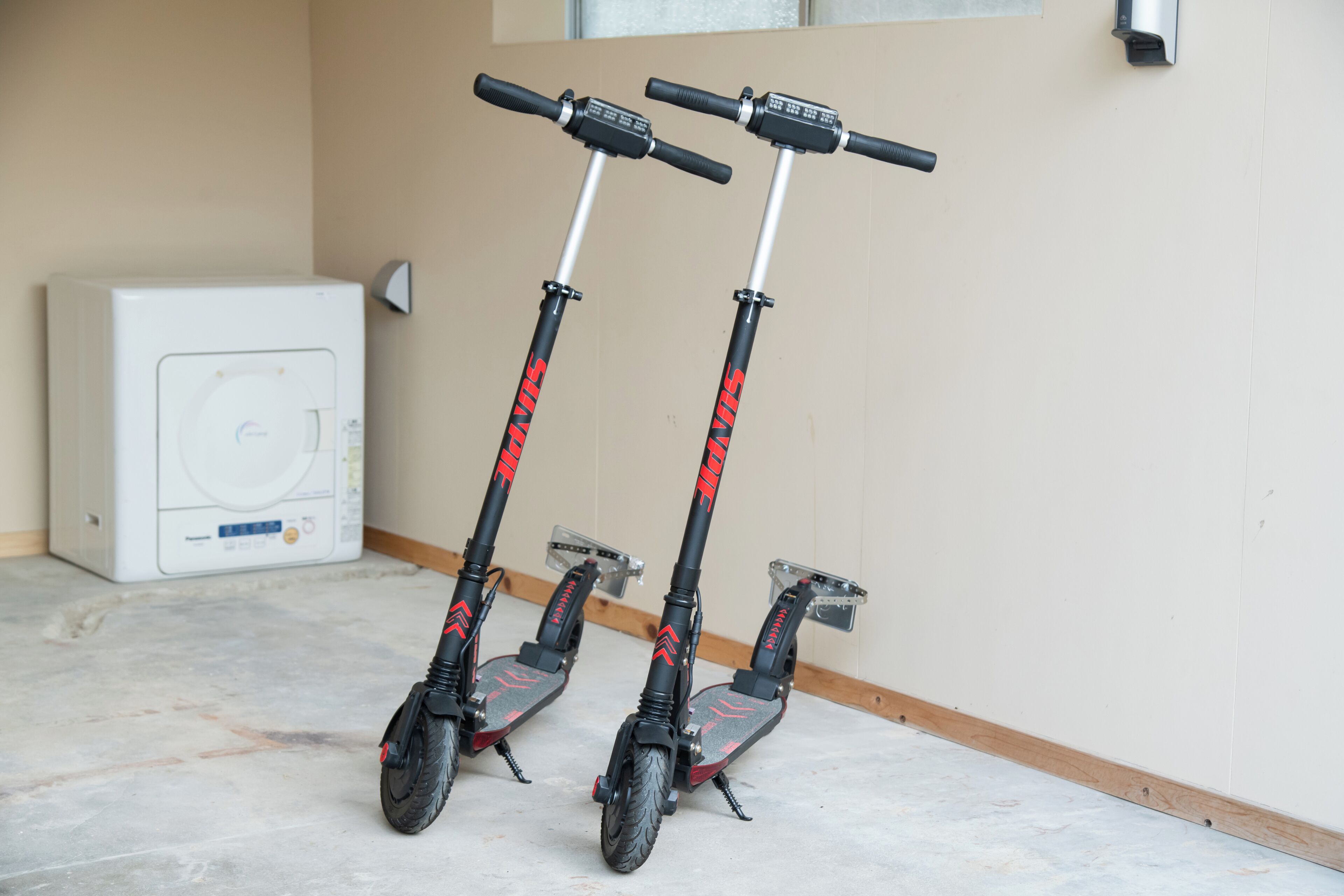 Dos scooters estacionados en el interior, una lavadora y un dispositivo montado en la pared.