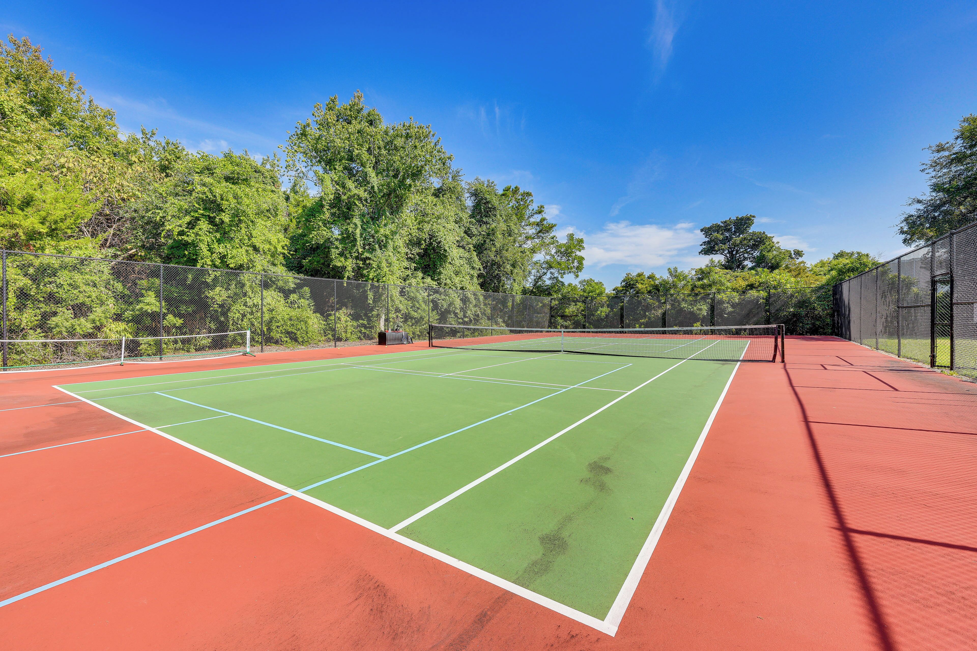 A tennis court with a net, surrounded by trees and a fence.